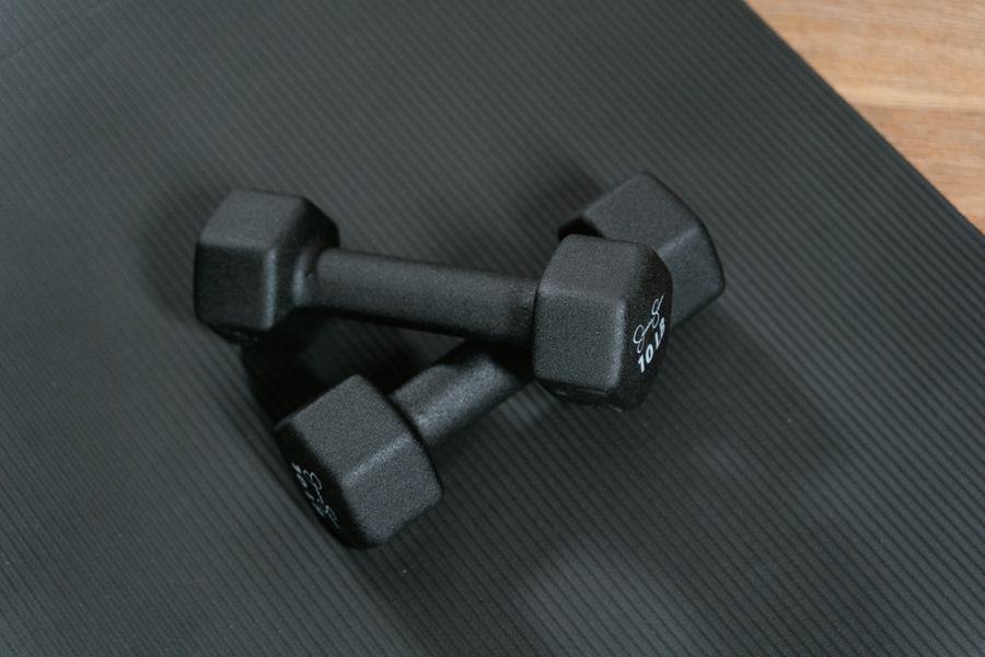 Two black dumbbells and an orange resistance band on a rustic wooden surface